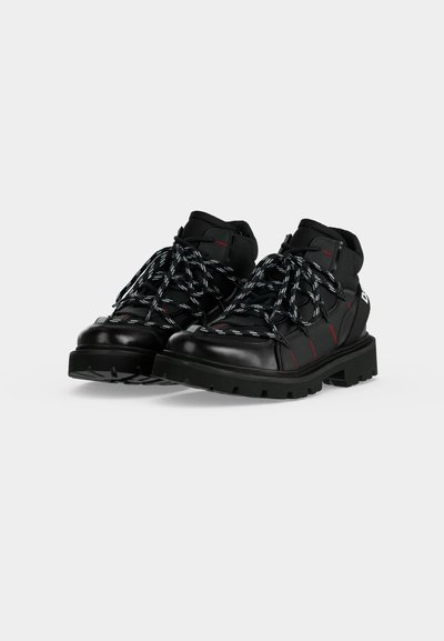 Paire de bottes de randonnée en cuir noir avec semelles épaisses et lacets à motifs noir et blanc sur un fond clair uni.