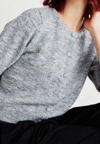 Gray knit cardigan with a round neckline embellished with beaded accents, featuring three buttons along the front for closure.