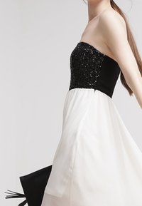 Strapless jurk met een aansluitende zwarte pailletten bodice, overgaand in een vloeiende witte rok, met een gladde textuur en zwarte accenten.
