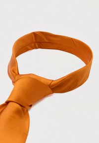 Pomarańczowy satynowy krawat o gładkiej fakturze i spiczastym końcu. Charakteryzuje się skręconym wzorem i spłaszczoną częścią węzła.