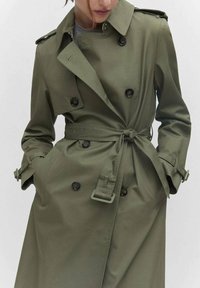 Olivgrüner Trenchcoat aus glattem Stoff, mit doppelt geknöpftem Verschluss, tailliertem Gürtel, Schulterklappen und aufgesetzten Taschen.