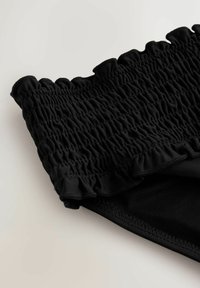 Sort bikinitrusse med smocket tekstur og flæsekant, lavet af elastisk stof med en glat overflade og sømløst design.