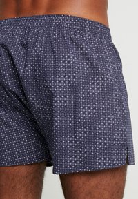 Marineblauwe boxershorts met een geometrisch wit patroon, elastische tailleband en zijsplitsen voor comfort. Gemaakt van lichte stof.