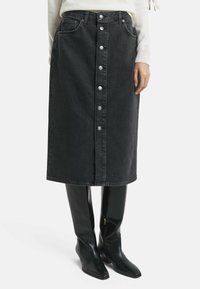 Gonna midi in denim nero con chiusura a bottoni frontale, due tasche e taglio dritto, abbinata a stivali neri lucidi al ginocchio.