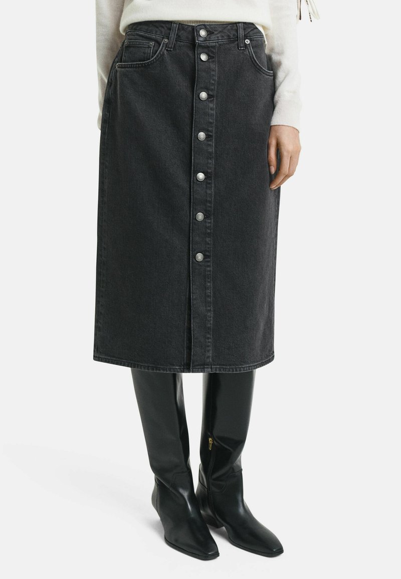 Gonna midi in denim nero con chiusura a bottoni frontale, due tasche e taglio dritto, abbinata a stivali neri lucidi al ginocchio.