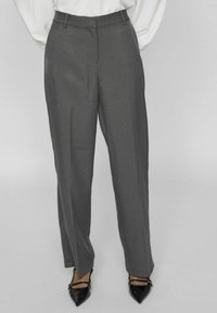 Pantalones grises de corte recto, con una textura suave y bolsillos laterales, combinados con tacones negros puntiagudos.