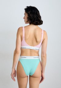 Podprsenka Calvin Klein v světle růžové barvě s nastavitelnými ramínky, v kombinaci s tyrkysovými kalhotkami s vysokým pasem a bílým logem na pásu.