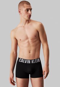 Svarte bomullsboxerbriefs med en hvit Calvin Klein-logo på livet. Glatt tekstur, tettsittende passform og kort benlengde.