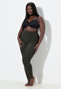 Hoch sitzende, olivgrüne Leggings aus dehnbarem Material, kombiniert mit einem schwarzen, formenden Bh, der eine glatte Textur und eine enganliegende Passform aufweist.