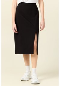 Svart midi kjol med hög slits, skräddarsydd design, slät textur och midjeband. Bärs med vita sneakers och ankelsockor.