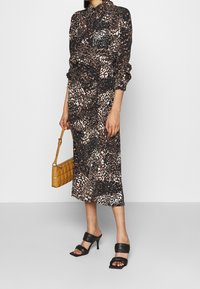 Långärmad klänning med krage i svart och brunt djurtryck. Har rynkad detaljering och är midi-lång. Kombineras med svarta klacksandaler och en beige väska.