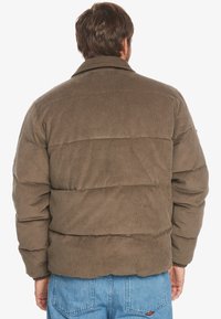 Brun kordfløjl pufferjakke med en struktureret overflade, der har vandret quiltede sektioner og en klassisk krave. Enkel design.