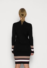 Robe pull noire à côtes avec des manches longues, présentant une silhouette ajustée, avec des accents rayés contrastés en beige, blanc et bordeaux aux poignets et à l'ourlet.