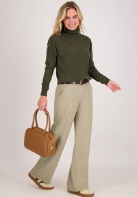 Vrouw die loopt in beige wijde broek, olijfgroene turtleneck, met een bruine handtas, en sneakers met een harige detail.