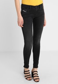 Jeans negros ajustados con una textura suave, un pequeño bolsillo frontal y dobladillo deshilachado. Combinados con tacones negros de tiras.