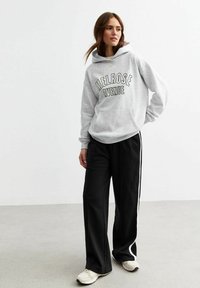 Gray hoodie with "MELROSE AVENUE" graphic, paired with black wide-leg pants featuring white side stripes, and light-colored sneakers.