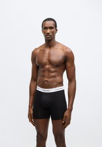 Boxeri negri cu talie elastică albă, cu logo-ul "Calvin Klein". Țesătură netedă, croială ajustată și lungime până la mijlocul coapsei.