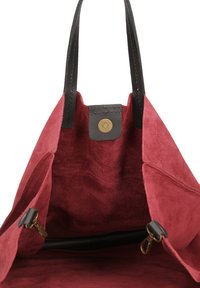 Borsa a tote in suede rosso con manici in pelle nera e chiusura a bottone in ottone. L'interno presenta una morbida texture con scomparti e una dettagli zip.