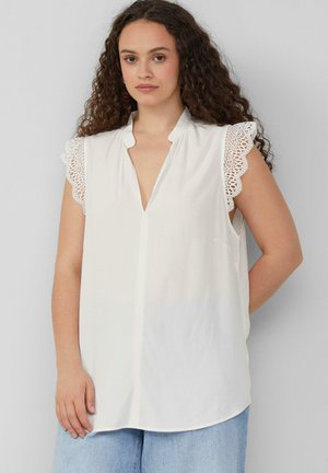 Blouse blanche sans manches avec un décolleté en V et des détails en dentelle sur les épaules. Tissu doux avec une coupe décontractée et un ourlet arrondi.