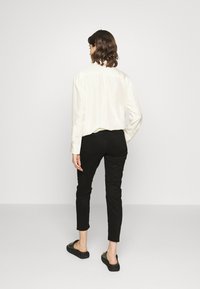 Chemise blanche à manches longues associée à un pantalon noir slim et des chaussures noires à enfiler. Tissu lisse, coupe ajustée et design minimaliste.