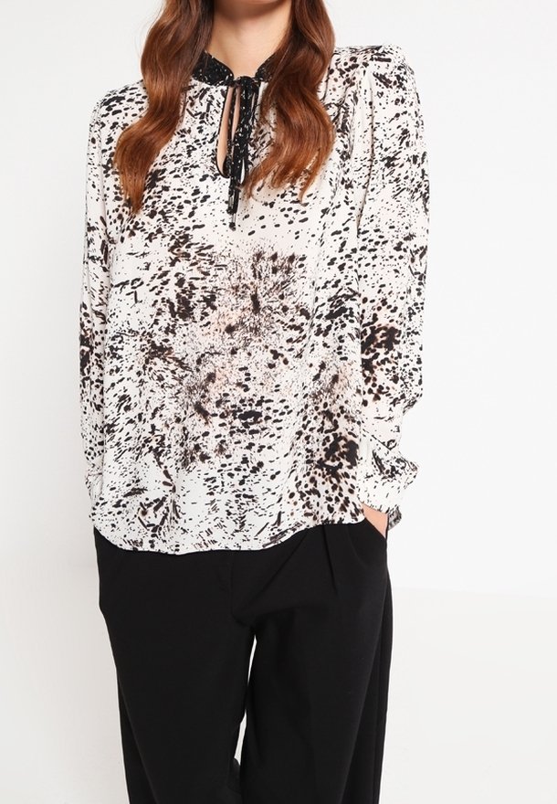 Blusa a maniche lunghe con motivo bianco e nero, colletto a occhiello e dettagli con cravatta nera, abbinata a pantaloni neri.