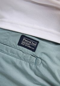 Chemise blanche rentrée dans un pantalon bleu clair avec une étiquette noire qui indique "Petrol Ind Denim Driven Since '89 Florida U.S.A."