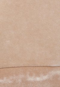 Tela de color beige claro con una textura tejida suave, que presenta un dobladillo acanalado. El material parece suave y ligeramente brillante en ciertas áreas.