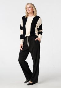 Zwart-crèmekleurige gestreepte trui, zwarte broek met elastische taille, zwart schoenen met spitse neus en studs, gladde texturen, comfortabele pasvorm.