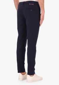 Pantaloni tailored blu navy in tessuto misto cotone, con una tasca posteriore e design slim fit. Indossati con sneakers bianche.