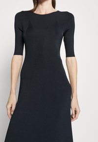 Robe en tricot bleu marine, avec un corsage ajusté, des manches courtes et une jupe évasée. Le motif côtelé texturé apporte un intérêt visuel.