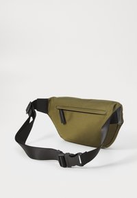 Olivegrünes Stoff-Fanny-Pack, ausgestattet mit einem verstellbaren schwarzen Gurt, einem oberen Reißverschluss und einer Rückentasche mit subtilen strukturierten Akzenten.