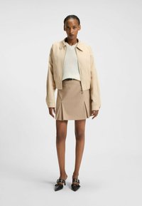 Beżowa kurtka typu cropped, biała dziana bluzka, brązowa spódnica w paski z plisami oraz czarne szpilki o spiczastym nosie z paskami i klamrami.