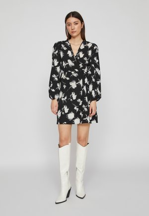 Black wrap dress with white floral pattern, long sleeves, and gathered waist. Paired with knee-high white pointed boots.