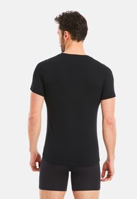 Black short-sleeve t-shirt made of soft material. Fitted design with a crew neck and curved hem. Worn with black shorts.