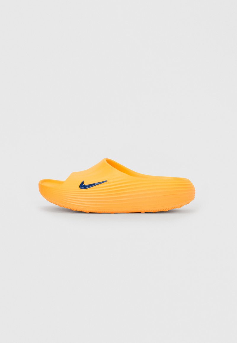 Pomarańczowa sandałka na wsuwanie z teksturowanymi rowkami i czarnym logo Nike na jednolitym jasnoszarym tle.