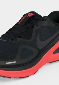 Μαύρο και κόκκινο αθλητικό παπούτσι Nike με μαύρα κορδόνια, λογότυπο Swoosh στο πλάι και κείμενο "RUN SECURELY 26" στην ετικέτα της γλώσσας.