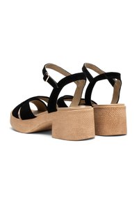 Czarne zamszowe sandały na masywnej, strukturze z brązowej platformy i zapięciu na kostkę. Otwarty nos z krzyżującymi się paskami dla dodatkowego wykończenia.