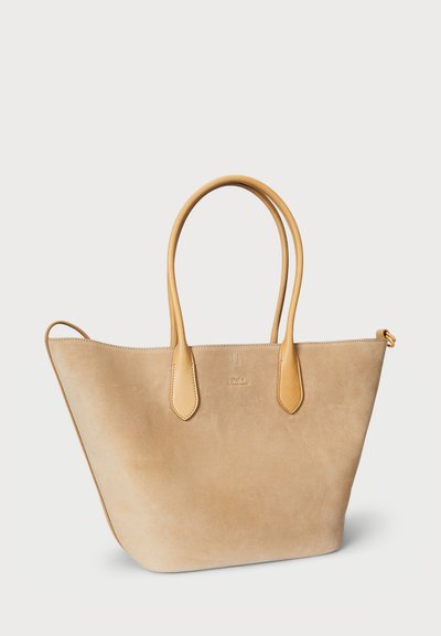 Borsa tote in suede beige con manici in pelle beige, apertura superiore ampia e dettaglio logo in rilievo discreto. Texture liscia, forma triangolare.