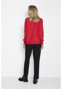 Roter gestrickter Pullover mit lockerer Passform, gerippten Bündchen und Saum, kombiniert mit tailoring schwarzen Hosen und schwarzen Slippern, aus der Rückenansicht betrachtet.