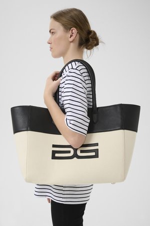 Canvas boodschappentas met een zwart faux leren bovenkant, een crème kleurig lichaam en een geperst "AG" logo. Voorzien van lange zwarte hengsels. Gestreepte shirt gedragen.