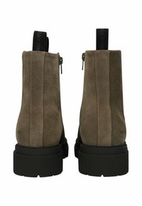 Ein Paar olivgrüne Wildlederstiefeletten mit schwarzen klobigen Gummisohlen und schwarzen Zuglaschen, von hinten auf einem weißen Hintergrund betrachtet.