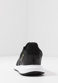 Svart träningssko med strukturerad design, vit sula och diskret guld-logotyp. Har en stickad ovandel och en rundad häl.