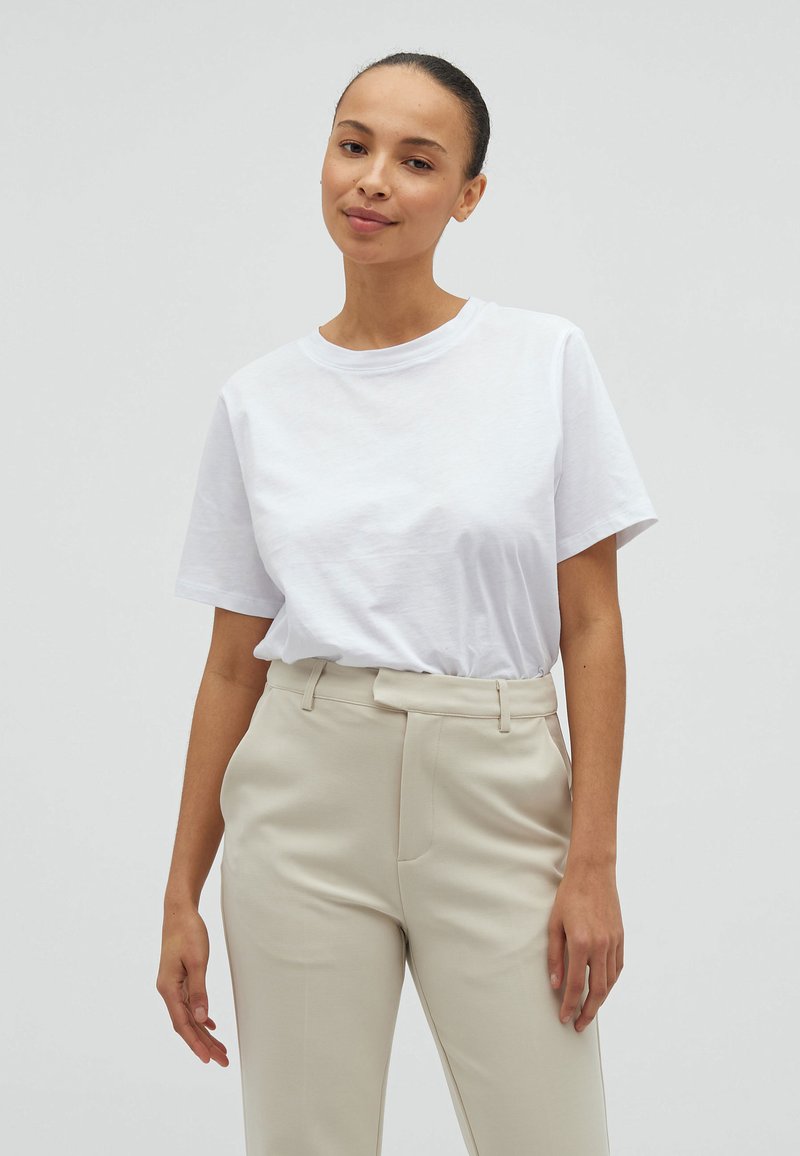 T-shirt bianco in cotone con maniche corte, scollatura rotonda e vestibilità comoda, abbinato a pantaloni beige chiaro su misura con tasche laterali.