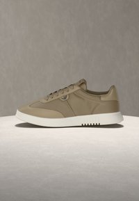 Μπεζ χαμηλό παπούτσι με κορδόνια στο μπροστινό μέρος, λείο σύνθετο επάνω μέρος και λευκή λαστιχένια σόλα σε ουδέτερο φόντο.