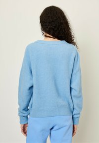 Ljusblå tröja i mjukt, fluffigt material med en avslappnad passform, ribbade ärmslut och nederkant, med en vid halsringning och sänka axlar.
