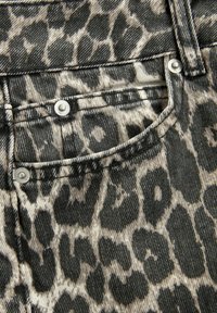 Tissu en denim à imprimé léopard avec un schéma de couleurs gris et noir, avec des accessoires en argent et un détail de poche avant.