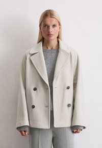 Veste en polaire légère grise à double boutonnage avec grands revers, deux boutons et un pull en tricot gris texturé en dessous. Coupe ajustée avec des manches droites.