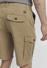 Shorts cargo beiges en coton. Avec des poches avant et arrière, des fermetures à bouton et une finition texturée. Décorés d'une patch de marque.