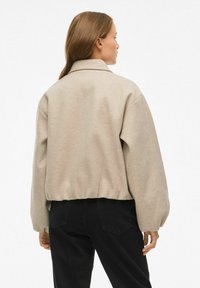 Bēša īsa jaka ar brīvu piegriezumu, kas aprīkota ar apkakli, pazeminātiem pleciem un elastīgu apakšmalu. Mīksts audums ar gludu tekstūru.