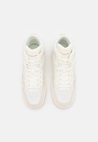 Wysokie sneakersy wykonane z białej skóry z jasnobeżowymi akcentami, z zaokrąglonym noskiem, perforowanym wzorem i białymi sznurówkami.